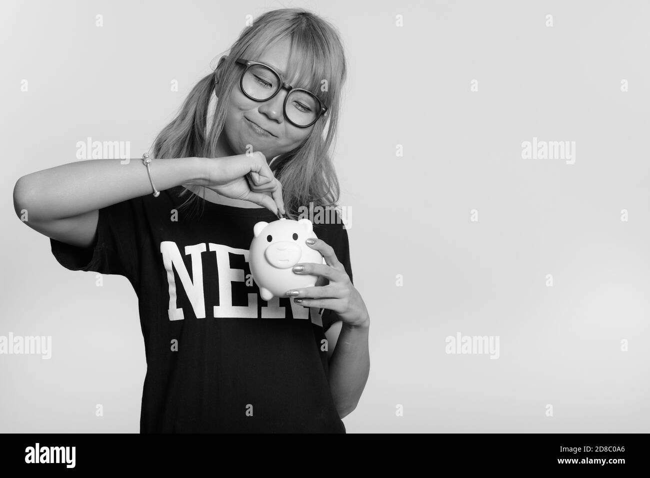 Giovani asiatici carino nerd donna mettendo moneta nel salvadanaio Foto Stock