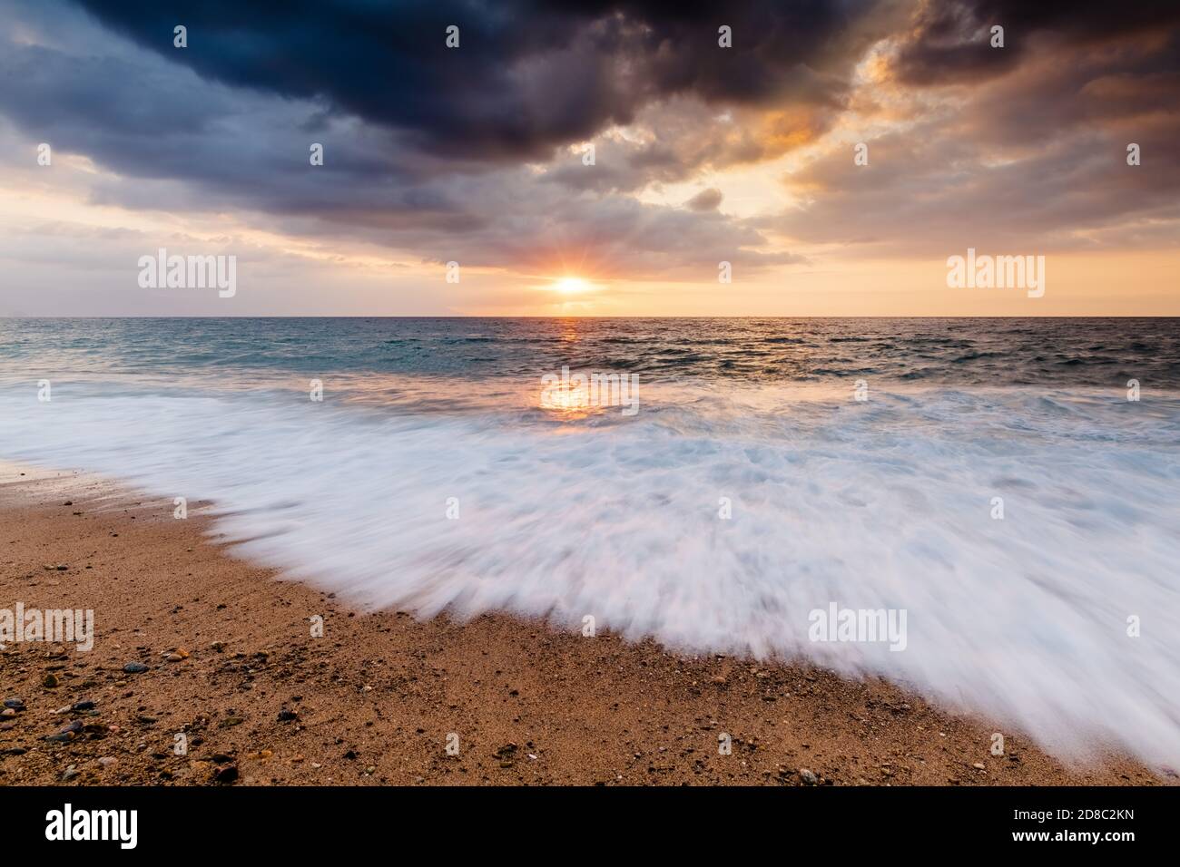 Un Rush of Wave Water arriva alla Shore AS Il sole si imposta sull'orizzonte dell'oceano Foto Stock