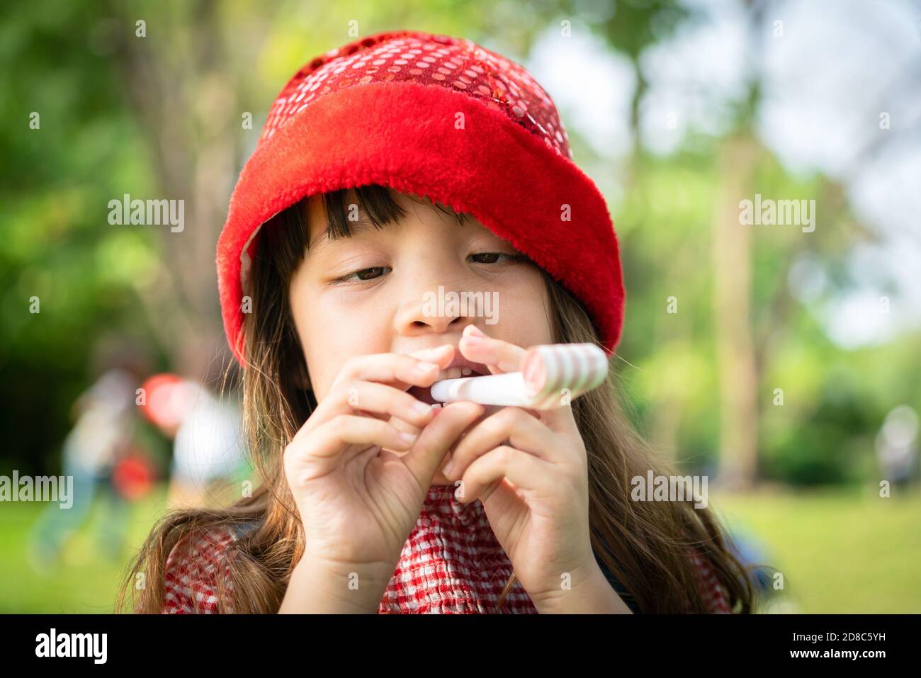 Piccolo felice School girl giocando parte soffiare il clacson per il suo compleanno nel giardino in estate. Stili di vita dell'infanzia concetto. Foto Stock