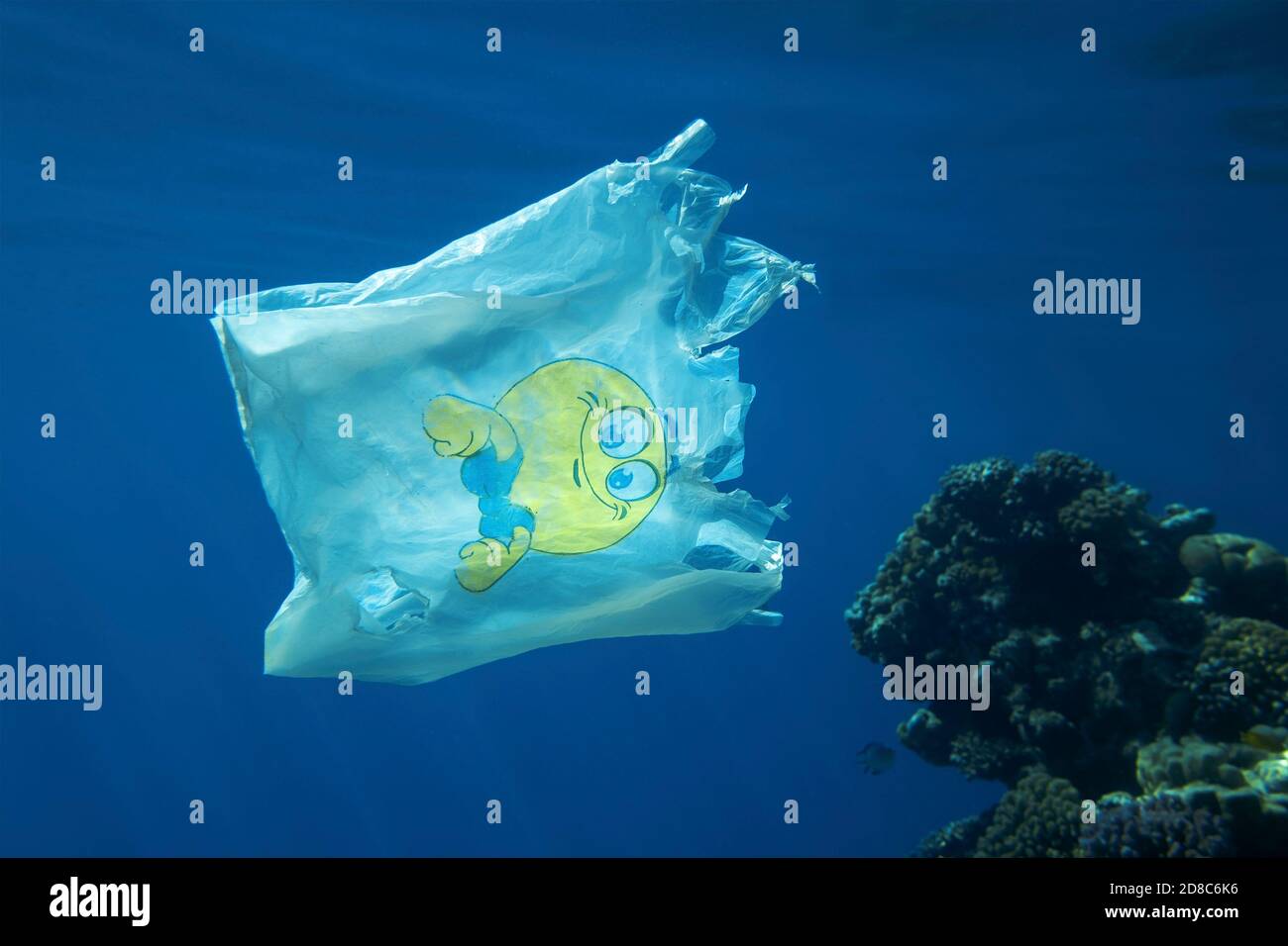 Inquinamento plastico, primo piano di sacchetto di plastica bianca con sorriso giallo che lentamente scivola sott'acqua sulla barriera corallina Foto Stock