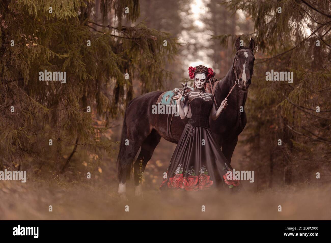 Giovane donna vestita come il simbolo messicano del giorno della calavera morta in un vestito nero che si posa in la foresta con un cavallo Foto Stock