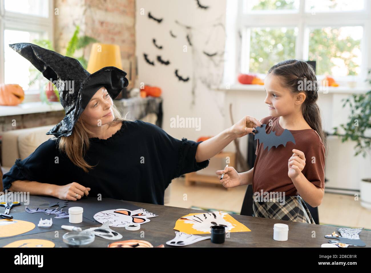 Giovane madre in streghe vestito seduto a tavola con Halloween Foto e creazione di costume a figlia per Halloween party Foto Stock