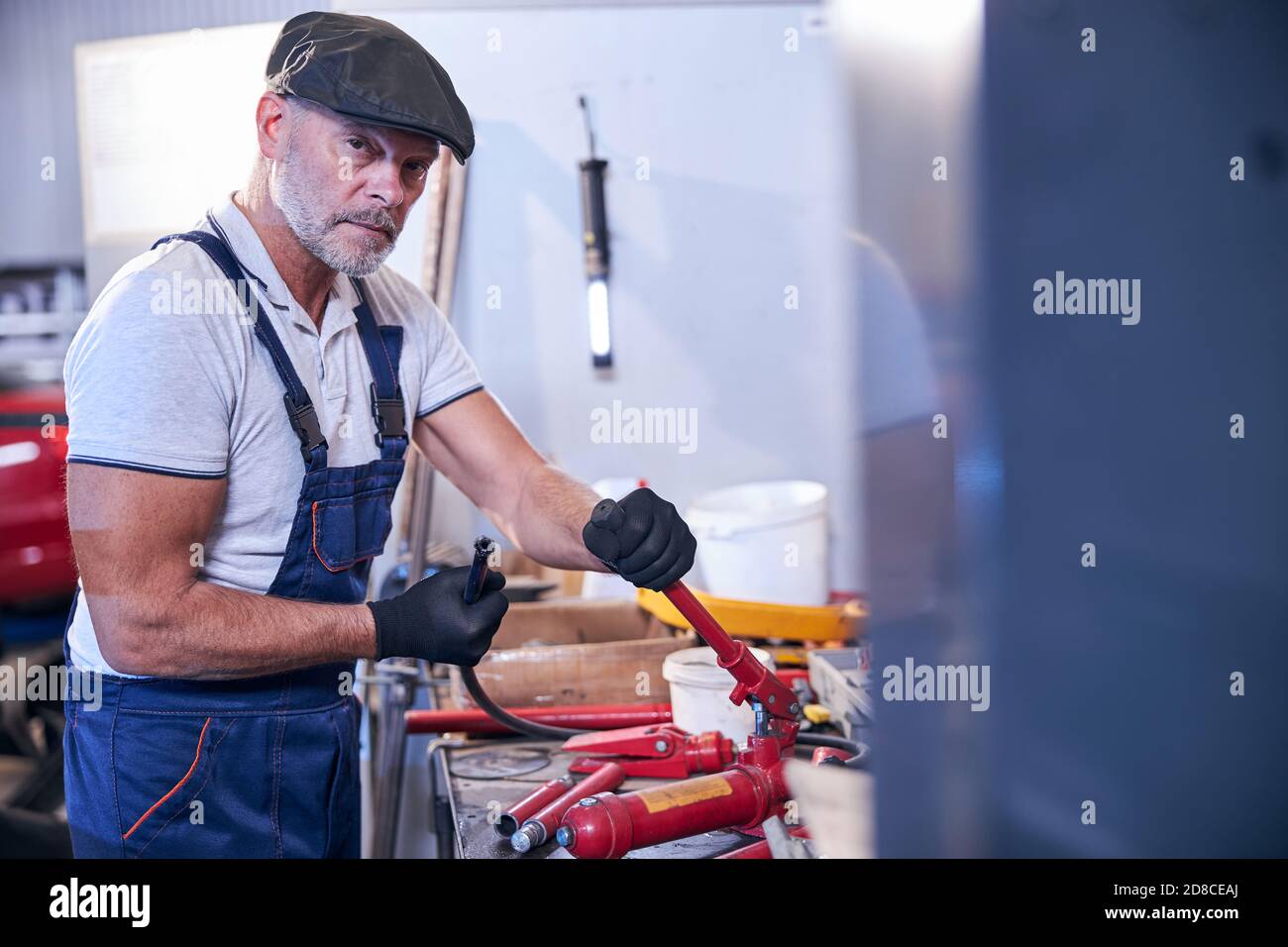 Lavoratore maschio con braccio che monta un martinetto idraulico portatile in garage Foto Stock