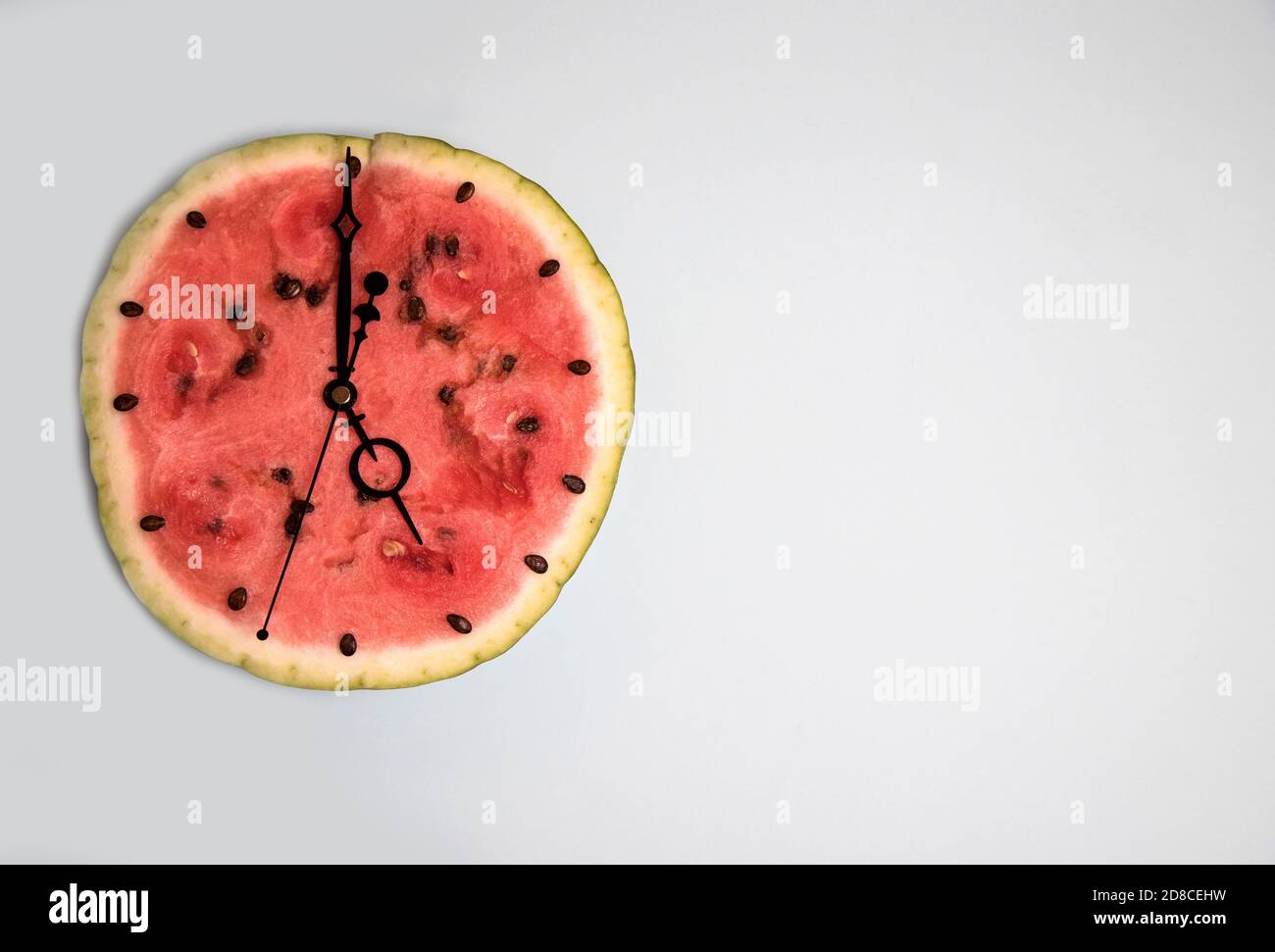 Fetta di anguria con frecce che mostrano le cinque sull'orologio, sfondo chiaro. Orientamento orizzontale. Spazio di copia Foto Stock