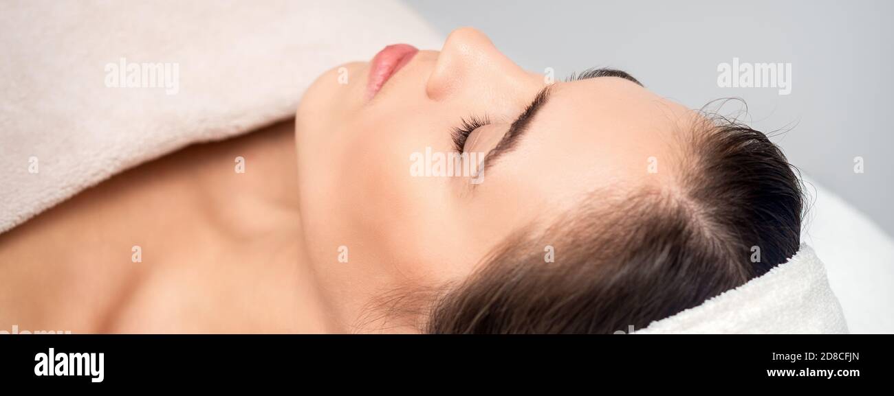 Vista laterale di giovane donna sdraiata su tavolo estetista con occhi chiusi in attesa di una procedura cosmetica in salone di bellezza Foto Stock