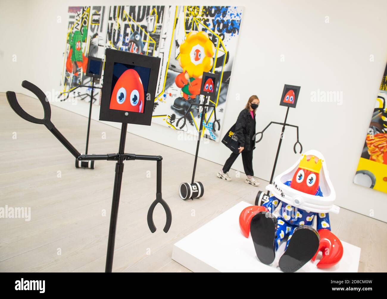 Un visitatore guarda le opere d'arte insieme ai robot telecomandati in un'anteprima stampa della mostra "Philip Colbert: Lobsteropolis" alla Saatchi Gallery di Londra, che offre al pubblico la possibilità di vedere le opere d'arte in situ o tramite i robot comodamente a casa propria. Foto Stock