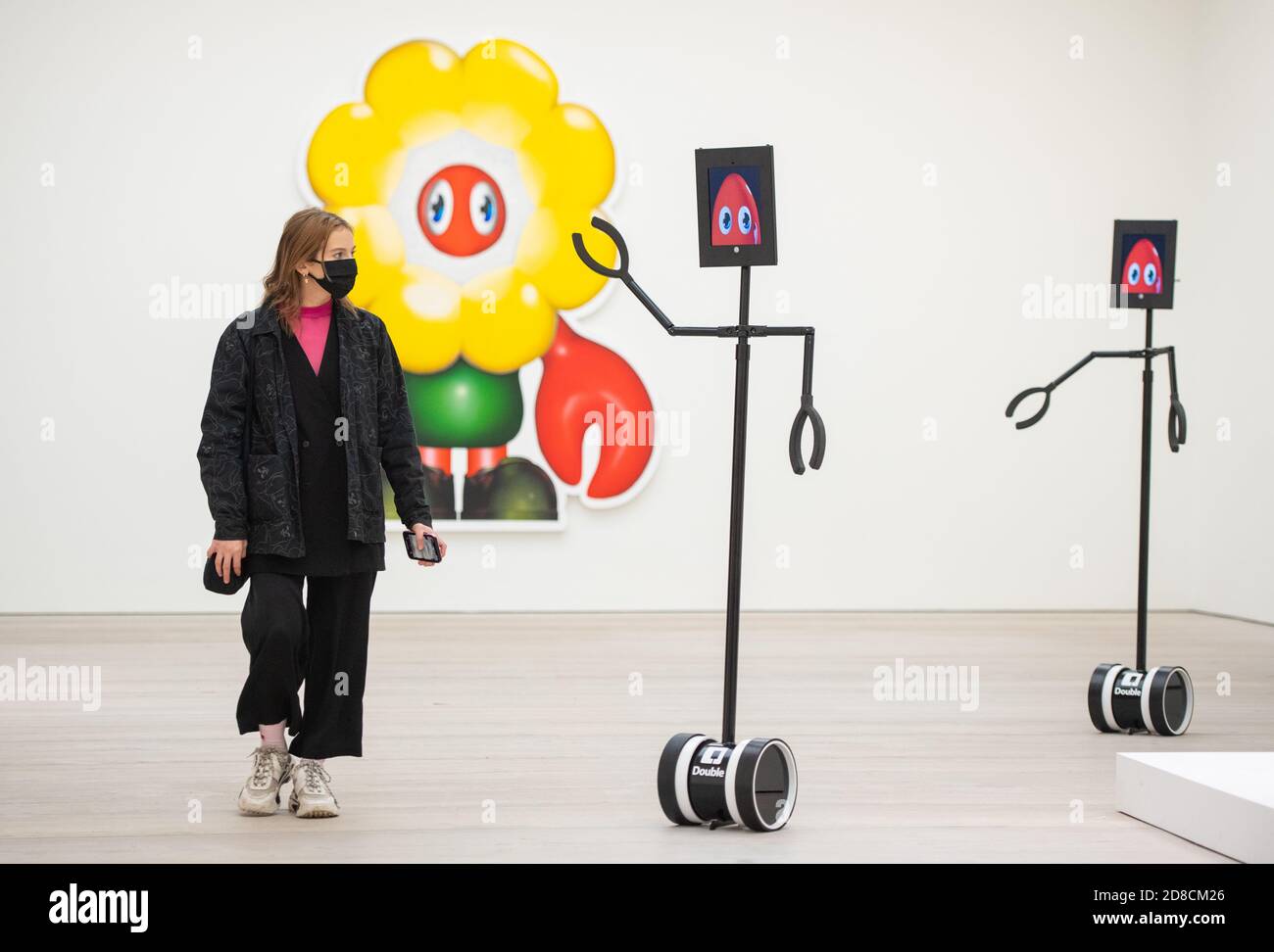 Un visitatore guarda le opere d'arte insieme ai robot telecomandati in un'anteprima stampa della mostra "Philip Colbert: Lobsteropolis" alla Saatchi Gallery di Londra, che offre al pubblico la possibilità di vedere le opere d'arte in situ o tramite i robot comodamente a casa propria. Foto Stock