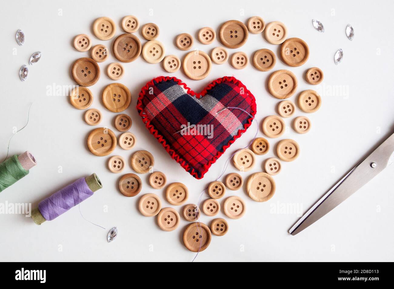 Posa piatta del kit di cucito con bottoni e cuscino dell'ago sulla forma del cuore su sfondo bianco, concetto di San Valentino Foto Stock