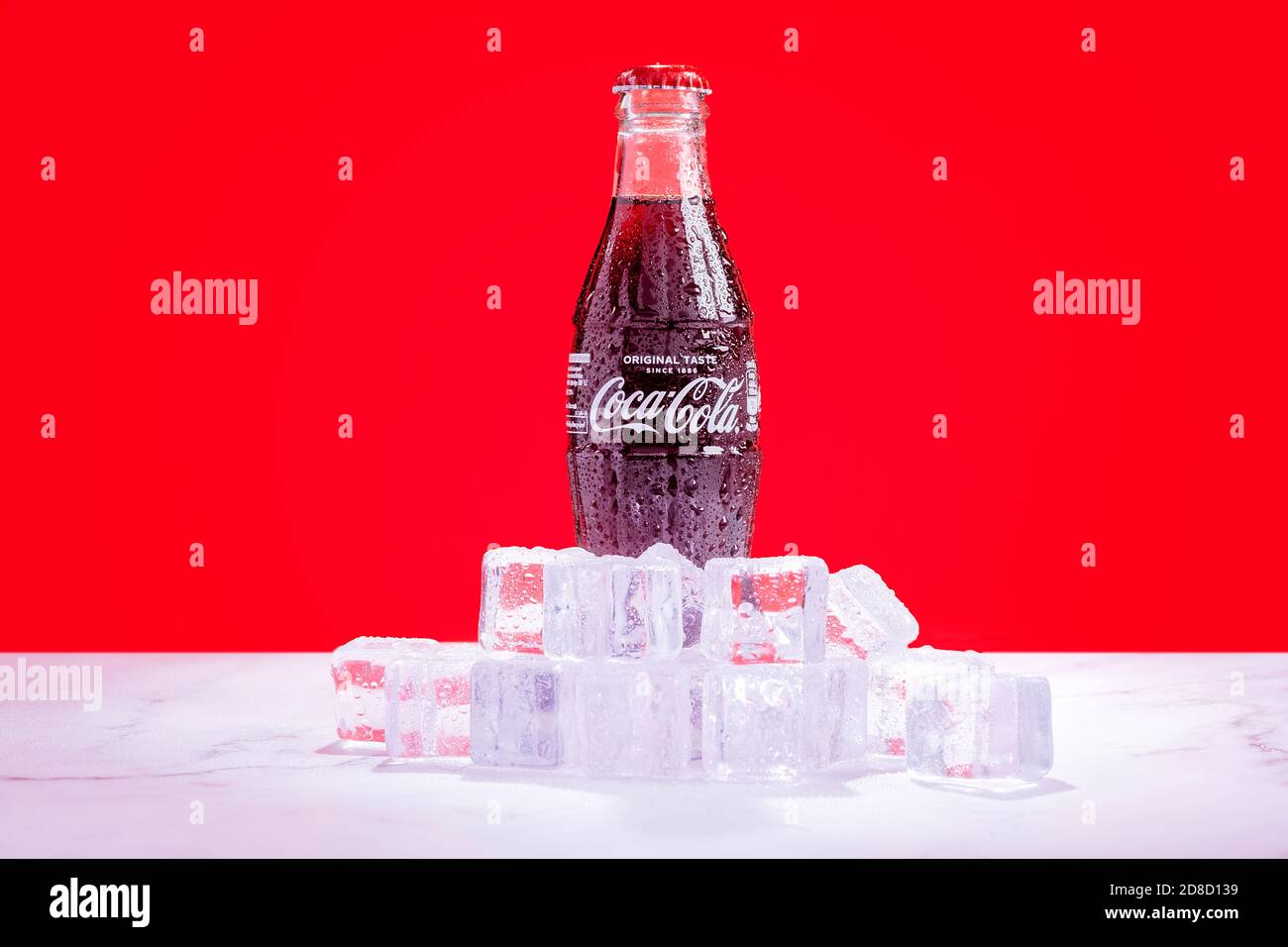 Londra, Regno Unito - Ottobre 29 2020: Una bottiglia di Coca Cola di vetro ghiacciato si trova in un mucchio di cubetti di ghiaccio con condensa su sfondo rosso. Foto Stock