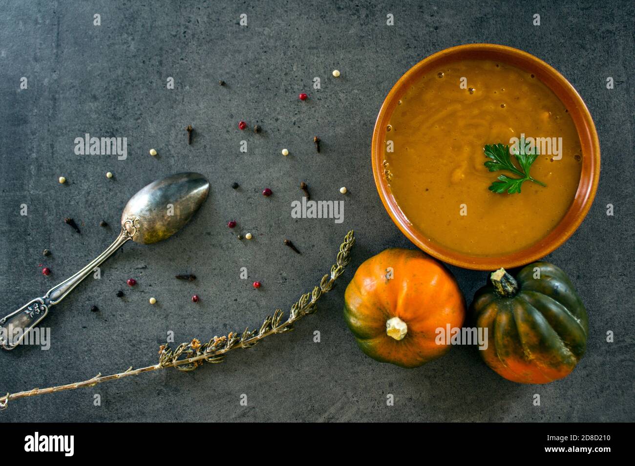 Foto dall'alto della ciotola con zuppa di zucca, squash di gemme,  rosmarino, pepe e cucchiaio d'argento. Sfondo grigio scuro con texture.  Concetto di alimentazione sana Foto stock - Alamy