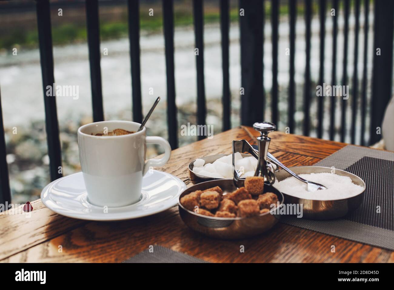 Una tazza di caffè e un piattino con zucchero su un tavolo di legno una terrazza che si affaccia sul pittoresco paesaggio con foresta e montagne fiume. Concetto wellbei Foto Stock