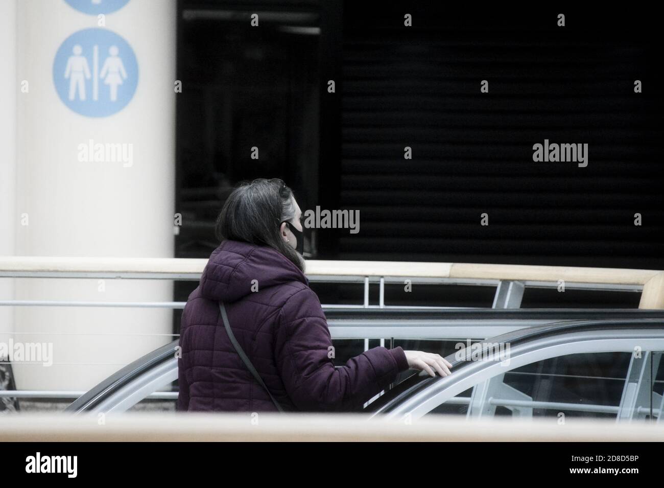 Donna nella scala mobile del centro commerciale con la sua maschera sul viso. Foto Stock