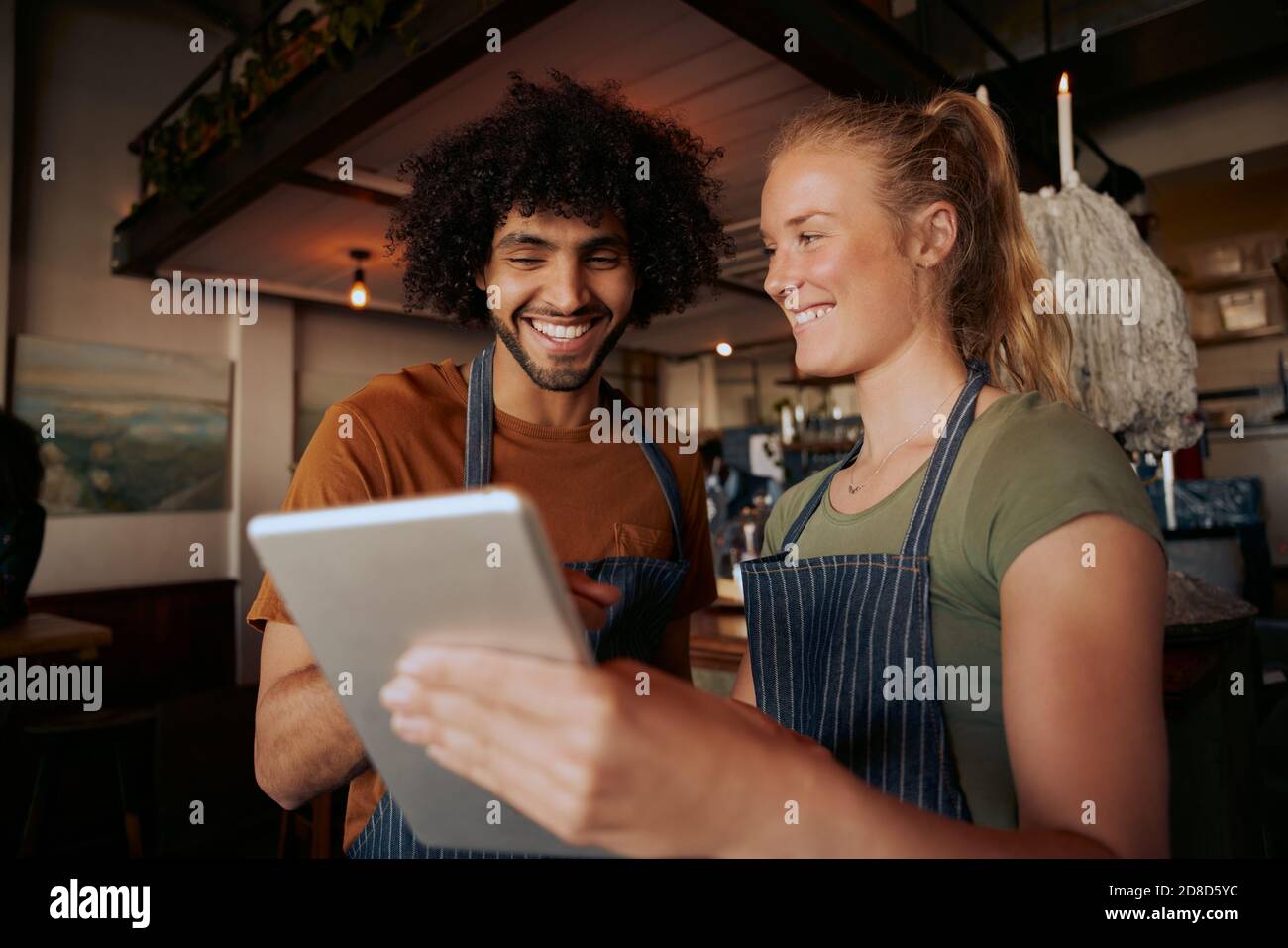 Ritratto di colleghi di sesso maschile e femminile che indossano grembiule e ridono durante la visione di video in un tablet digitale al bar Foto Stock