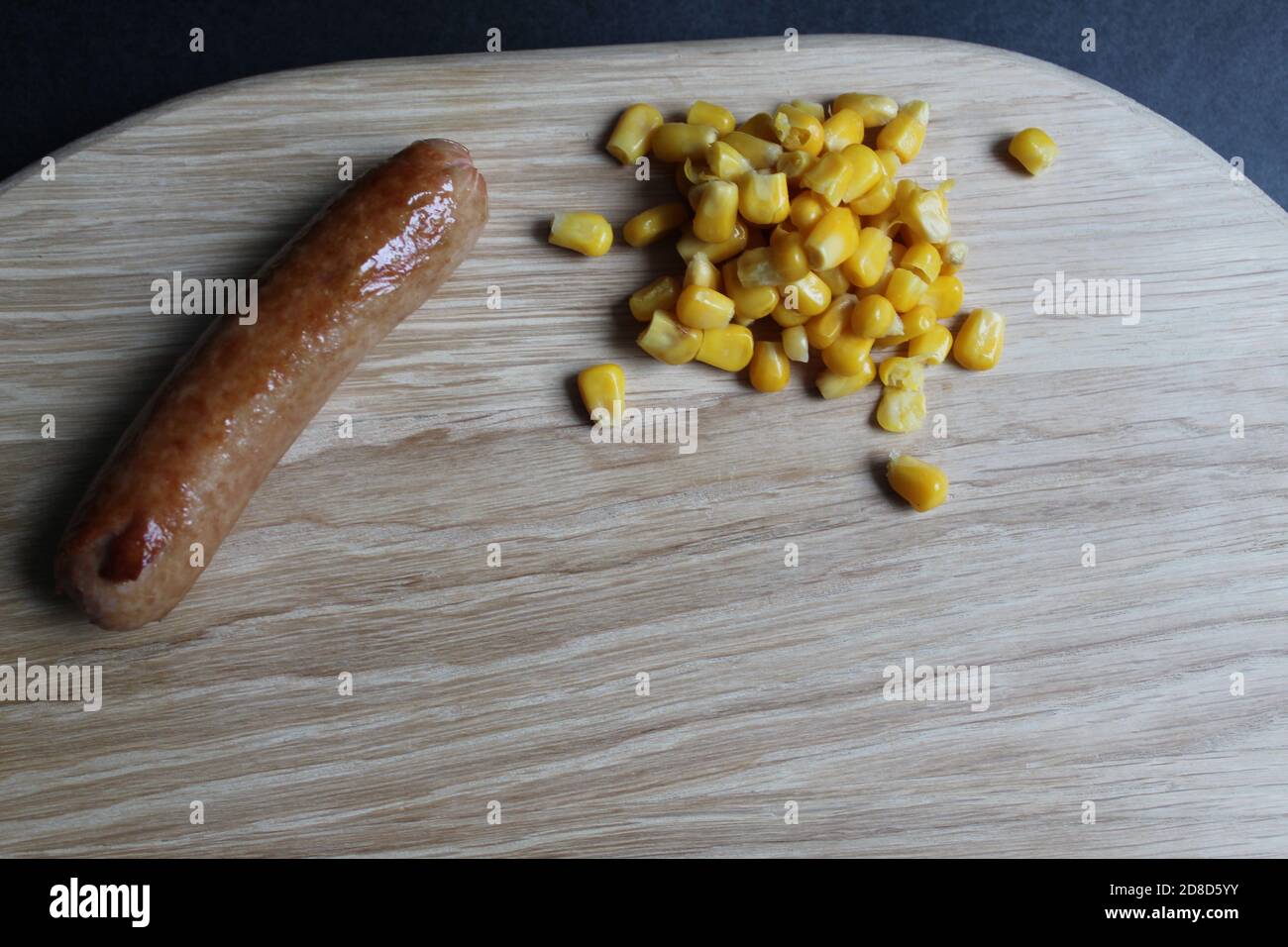 Colazione, pranzo o cena, mais dolce e salsiccia alla griglia La salsiccia si trova su un vassoio di legno di supporto per asse su un sfondo nero scuro dello spazio di copia Foto Stock