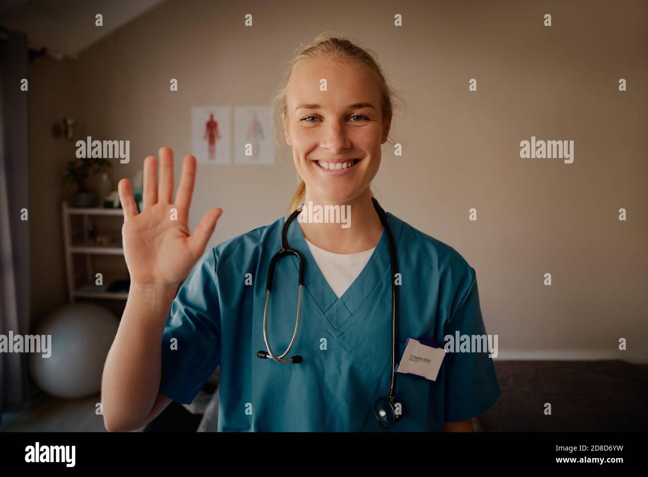 Ritratto di sorridente bella giovane infermiera che agita la mano con stetoscopio Foto Stock