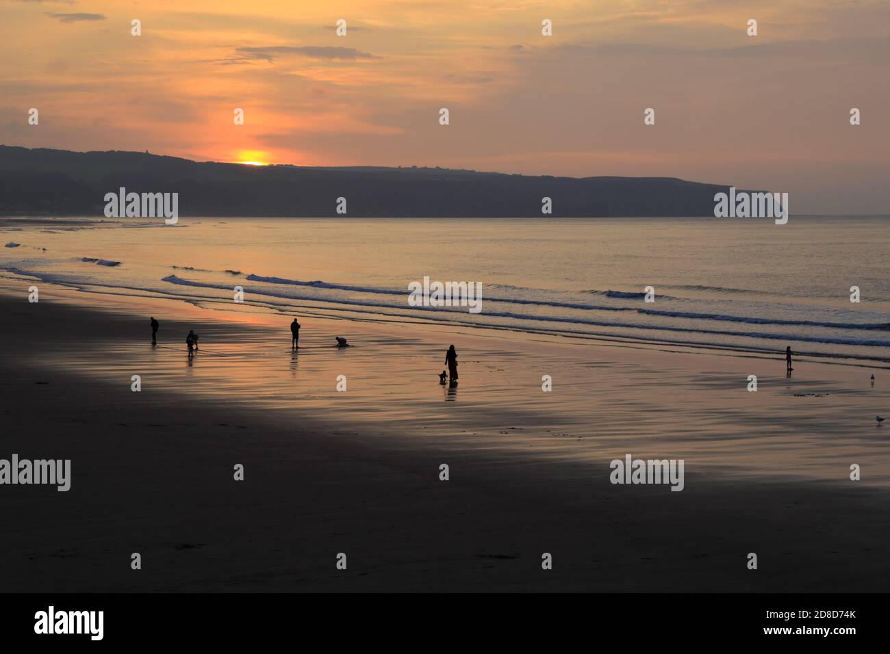 Sagome di persone che camminano sulla spiaggia di Whitby mentre il sole tramonta sulla costa orientale, Whitby, North Yorkshire, Inghilterra, Regno Unito. Foto Stock