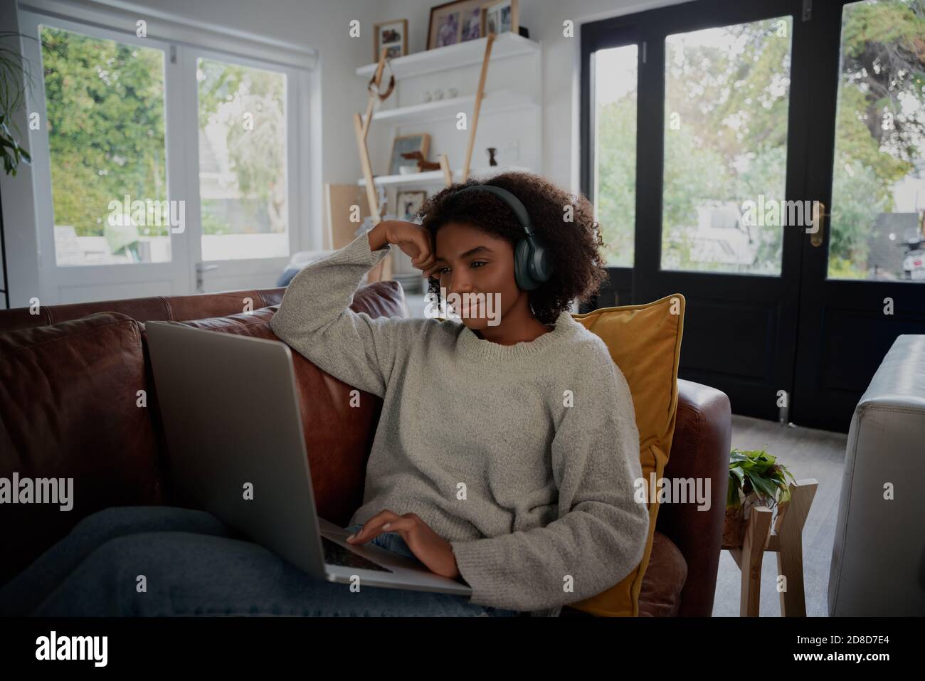 Giovane studente nero che si gode vacanza blocco guardando video su computer portatile con cuffie a casa Foto Stock