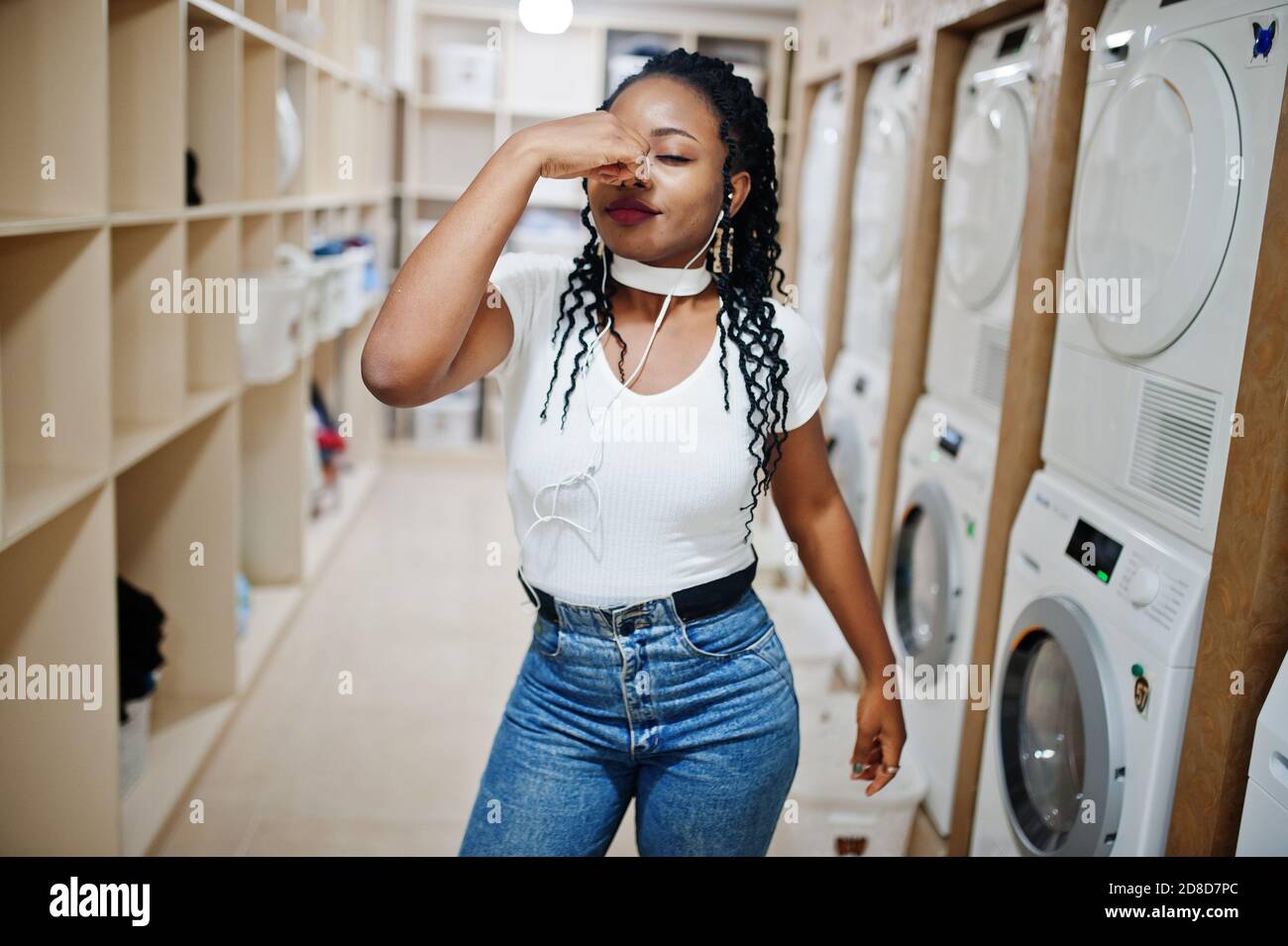 Qui smels cattivo. Triste e delusa donna afroamericana vicino lavatrice nella lavanderia self-service. Foto Stock