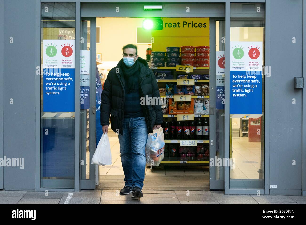 Un uomo lascia un supermercato Tesco che indossa una maschera chirurgica per il viso dove è in funzione un sistema di semafori a Cardiff, Galles, Regno Unito. Foto Stock
