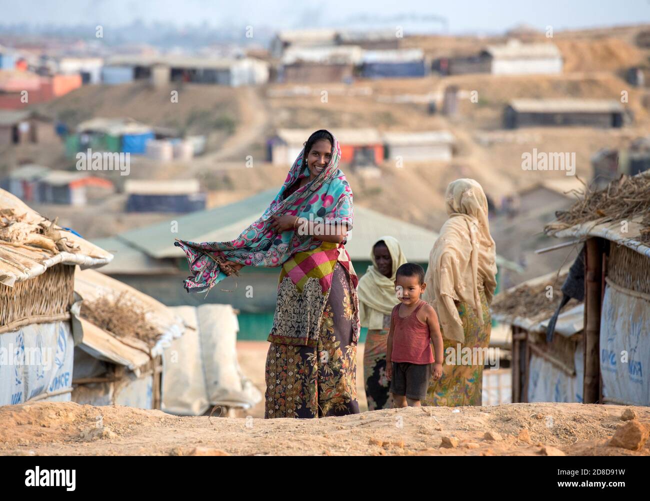 La gente di Rohingya cammina intorno mentre i rifugi sono visti dietro loro al campo profughi di Kutupalong a Maynar Guna, vicino a Bazar di Cox, Bangladesh il 16 aprile 2018. I Rohingya, fuggiti dall'oppressione in Myanmar, cercano di vivere in condizioni difficili in insediamenti improvvisati fatti di bambù, adobe o nylon nel campo profughi di Kutupalong. Oltre 650,000 Rohingya hanno attraversato il confine con il Bangladesh dall’agosto dello scorso anno, in fuga dalle violenze. Foto Stock