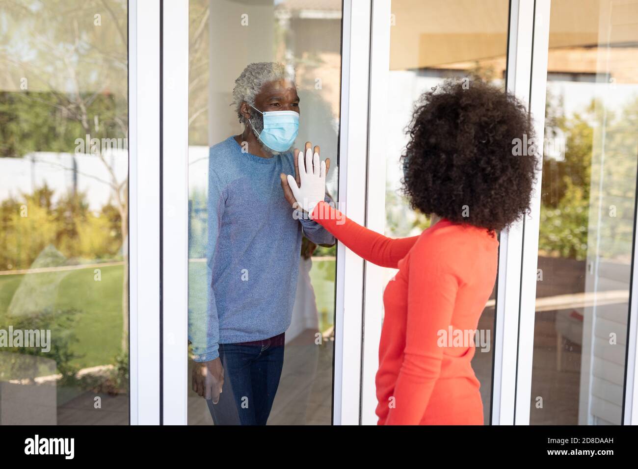 Uomo anziano che indossa una maschera a contatto reciproco attraverso la finestra vetro Foto Stock