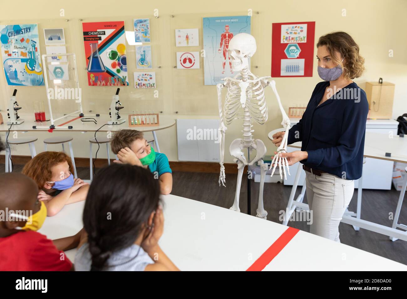 Insegnante di sesso femminile che indossa maschera di faccia usando il modello di scheletro umano a. insegnare agli studenti in classe Foto Stock