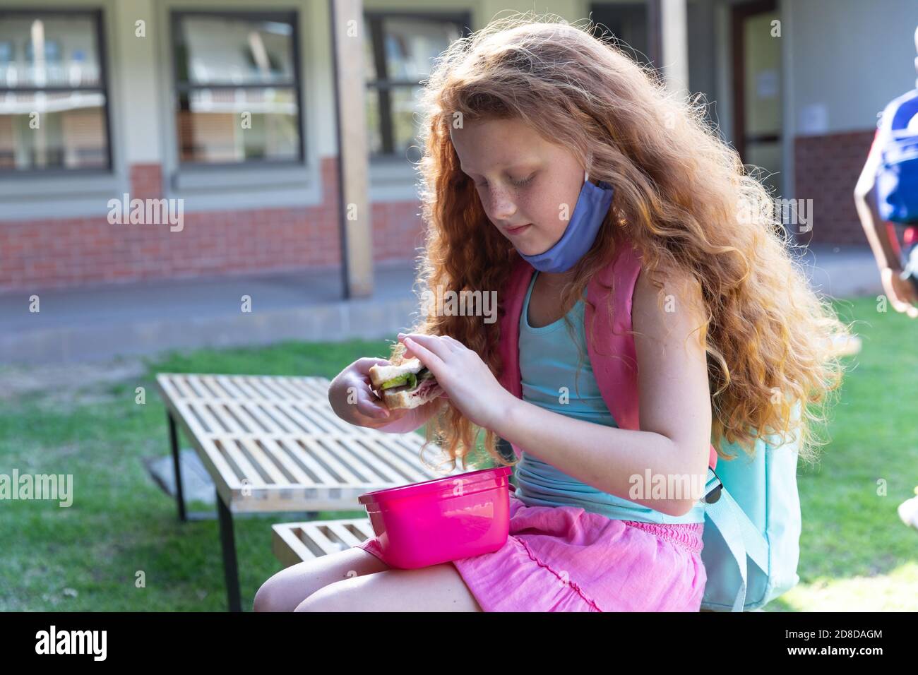 Ragazza che mangia il pranzo dalla scatola di tiffin mentre si siede sulla panchina nel parco a scuola Foto Stock