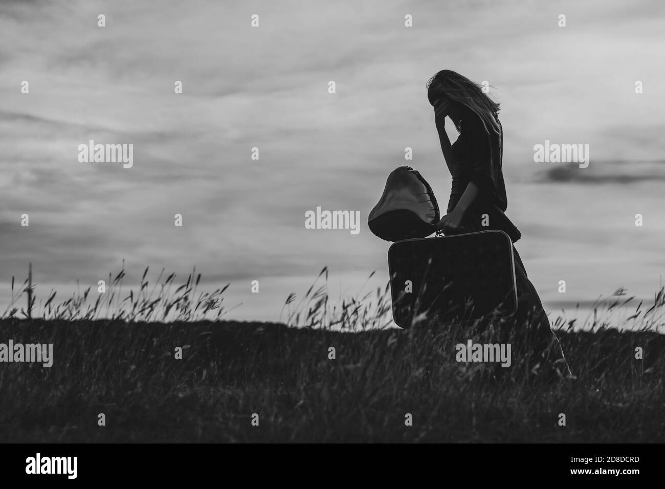 Donna triste che tiene valigia e palloncino a forma di cuore nella natura. Foto in bianco e nero. Foto Stock