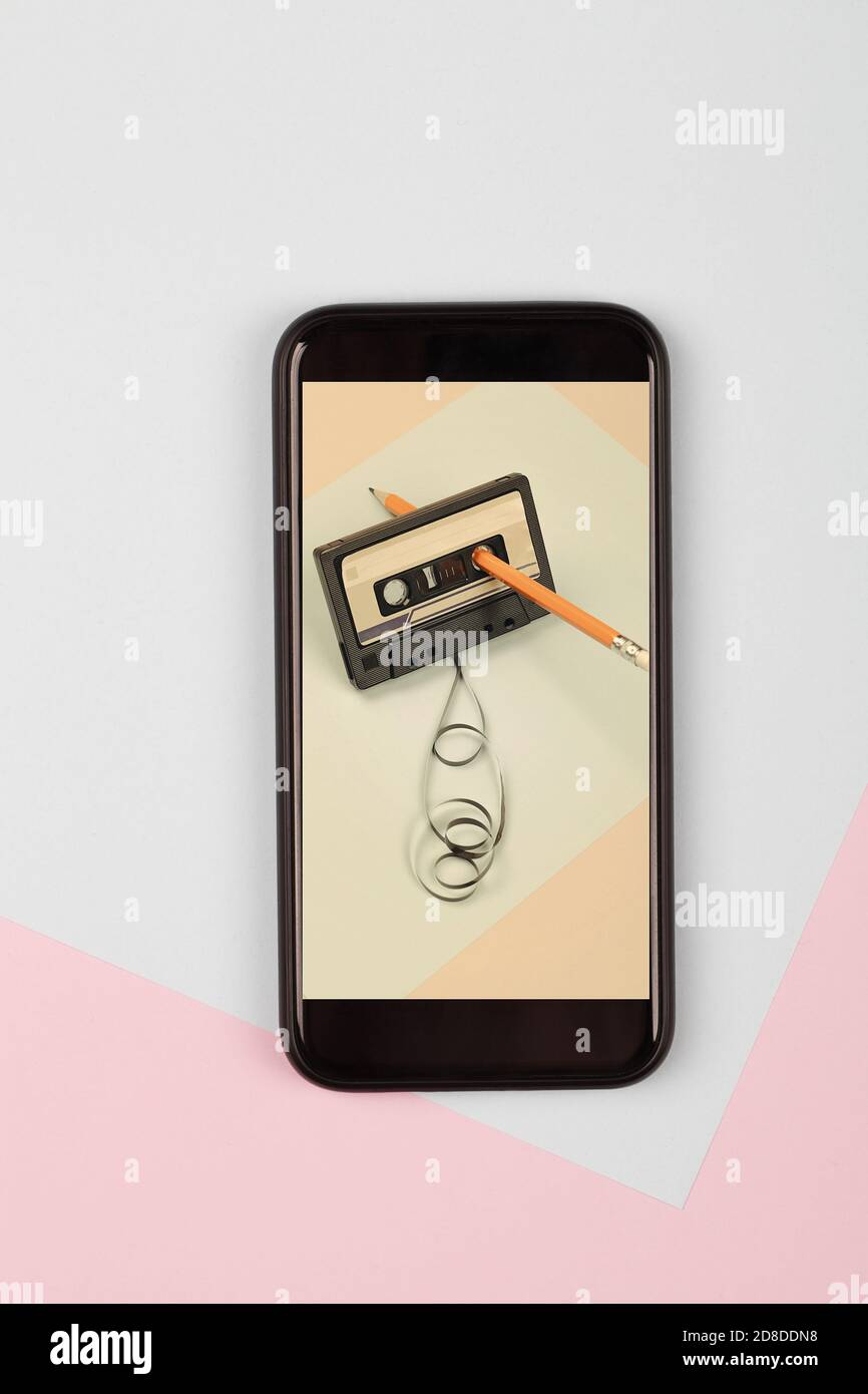 audiocassetta fotografica con nastro aggrovigliato su sfondo blu con matita sul nuovo cellulare, composizione minimalista. concetto retrò e moderno Foto Stock