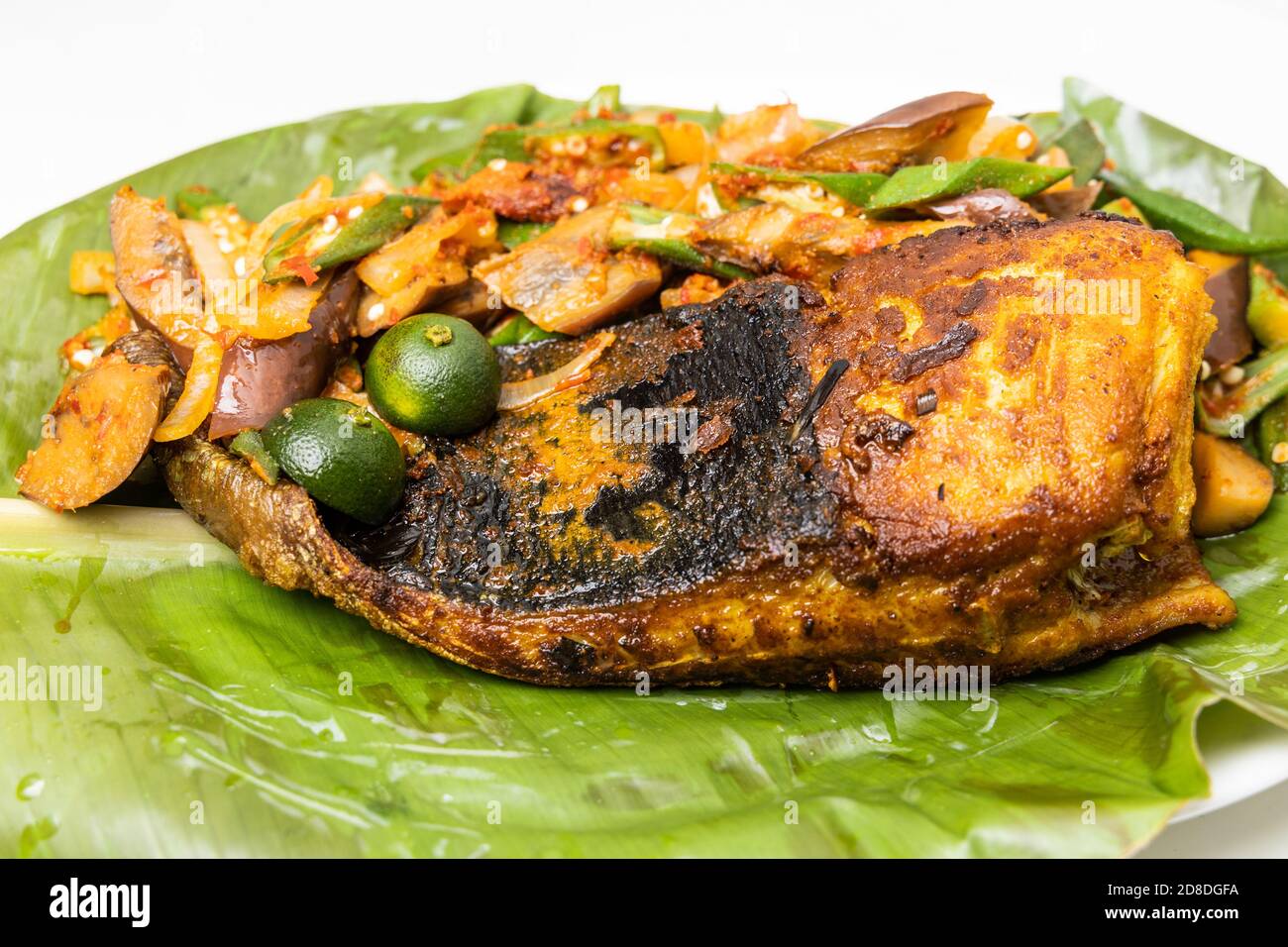 Primo piano del famoso pesce di razza alla griglia con spezie e verdure servito su foglia di banana Foto Stock