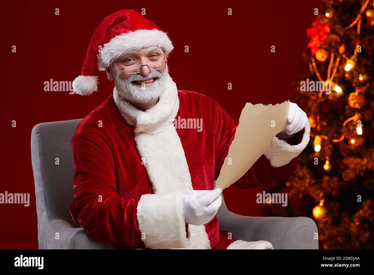 Ritratto di Santa sorridente alla macchina fotografica mentre si siede sulla poltrona E leggere la lettera di Natale Foto Stock