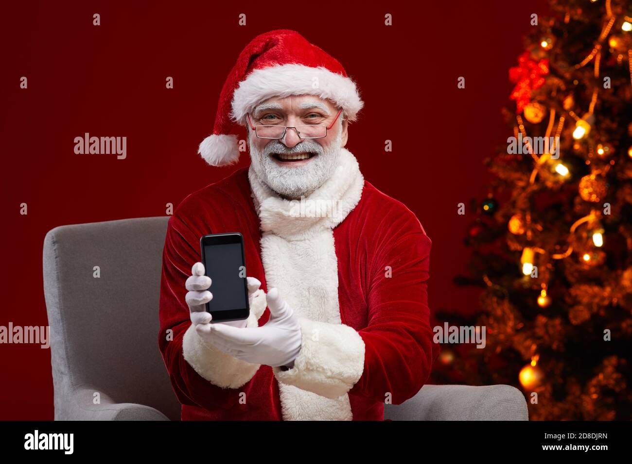 Ritratto di Babbo Natale in occhiali sorridenti alla macchina fotografica tenere il telefono cellulare nelle mani Foto Stock