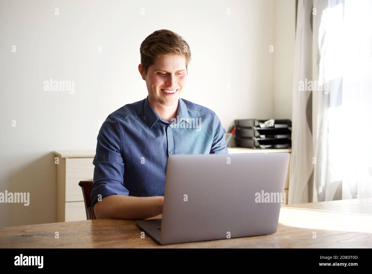 Ritratto di giovane uomo d'affari seduto alla scrivania e su cui lavorare computer portatile Foto Stock