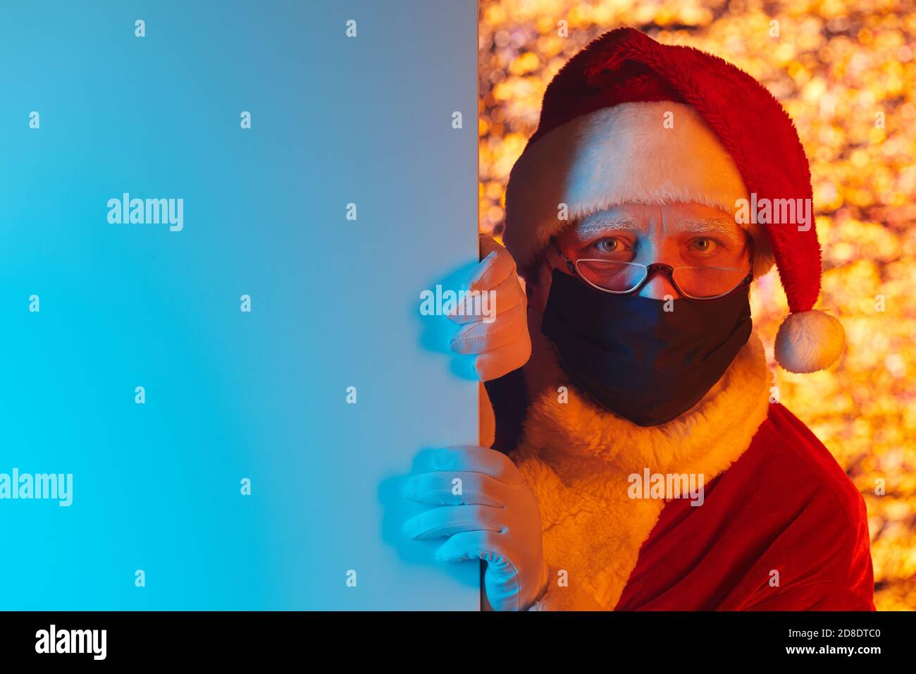 Ritratto di Babbo Natale in cappello e maschera protettiva guardando la fotocamera dietro la parete Foto Stock
