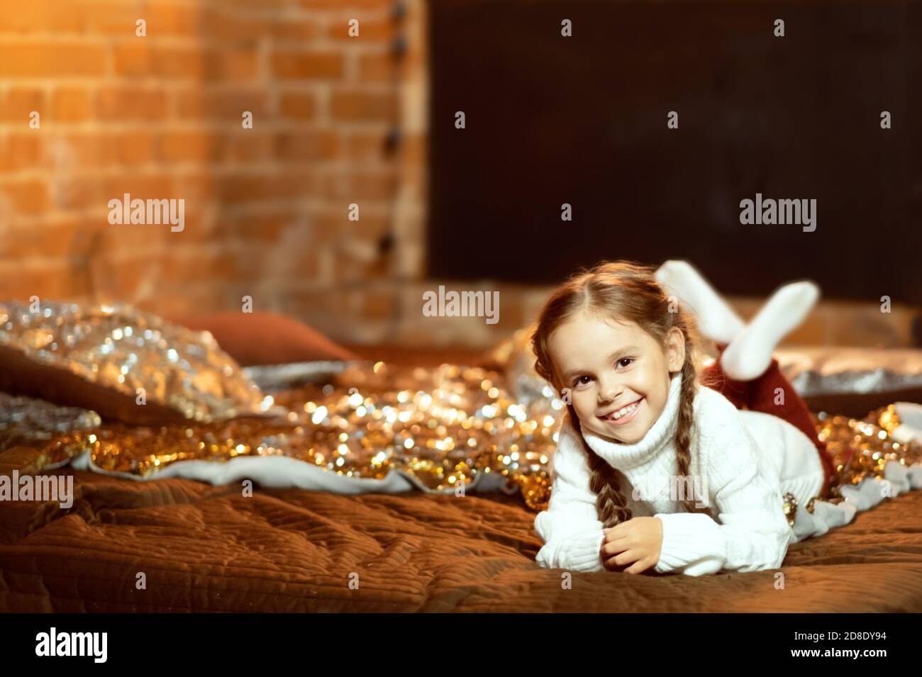 bambina in un vestito di natale. ragazza giace sul letto e sorride. Accogliente foto della casa. Comfort natalizio a casa Foto Stock