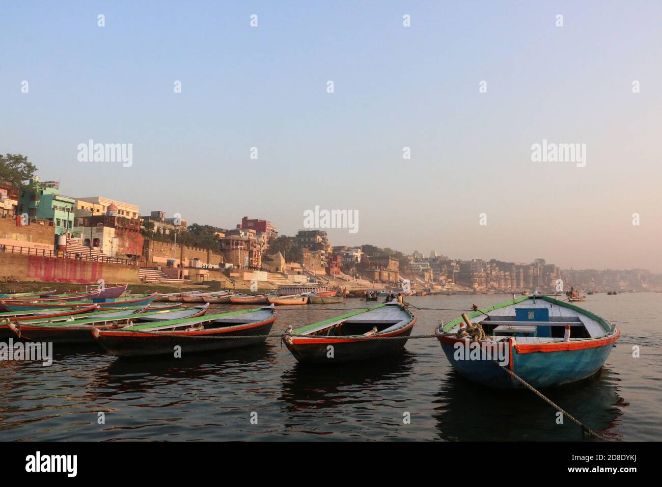 Barche ormeggiate fiancheggiate sul Gange con edifici Varanasi in background e spazio per la copia Foto Stock