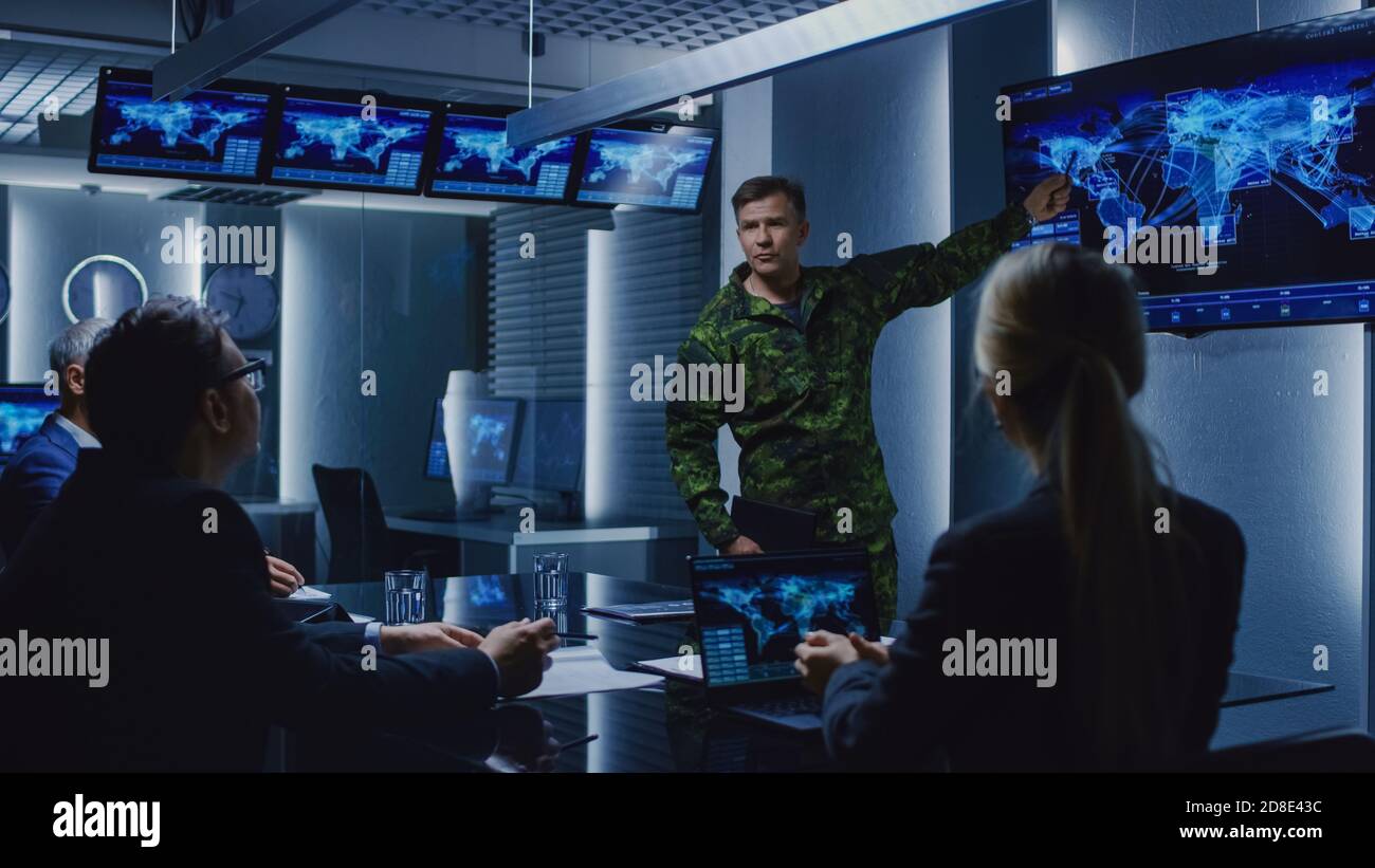 High-Ranking Military Man tiene un briefing a un team di agenti governativi e politici, mostra le riprese di sorveglianza satellitare. Foto Stock
