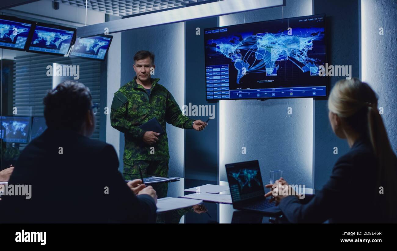 High-Ranking Military Man tiene un briefing a un team di agenti governativi e politici, mostra le riprese di sorveglianza satellitare. Foto Stock