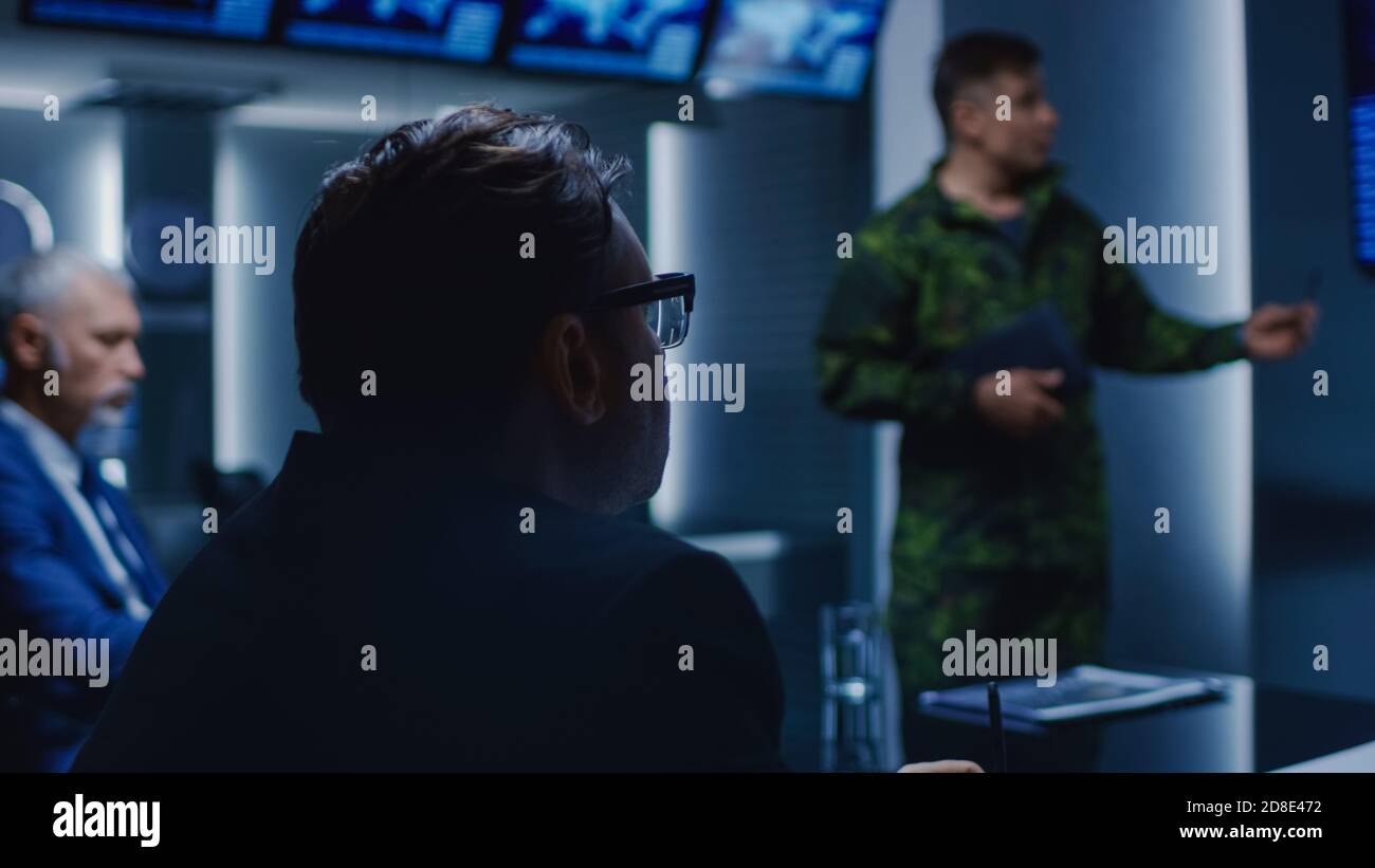 High-Ranking Military Man tiene un briefing a un team di agenti governativi e politici, mostra le riprese di sorveglianza satellitare. Foto Stock