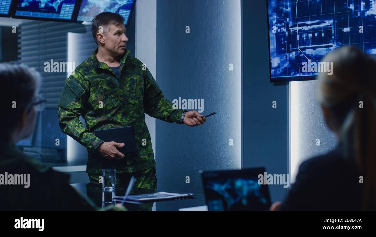High-Ranking Military Man tiene un briefing a un team di agenti governativi e politici, mostra le riprese di sorveglianza satellitare. Foto Stock
