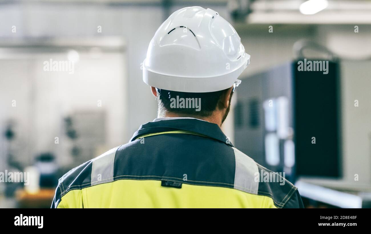 Indietro Vista Foto dell'ingegnere industriale che indossa indumenti protettivi Attraversa il moderno stabilimento di produzione con macchine automatiche in funzione Foto Stock