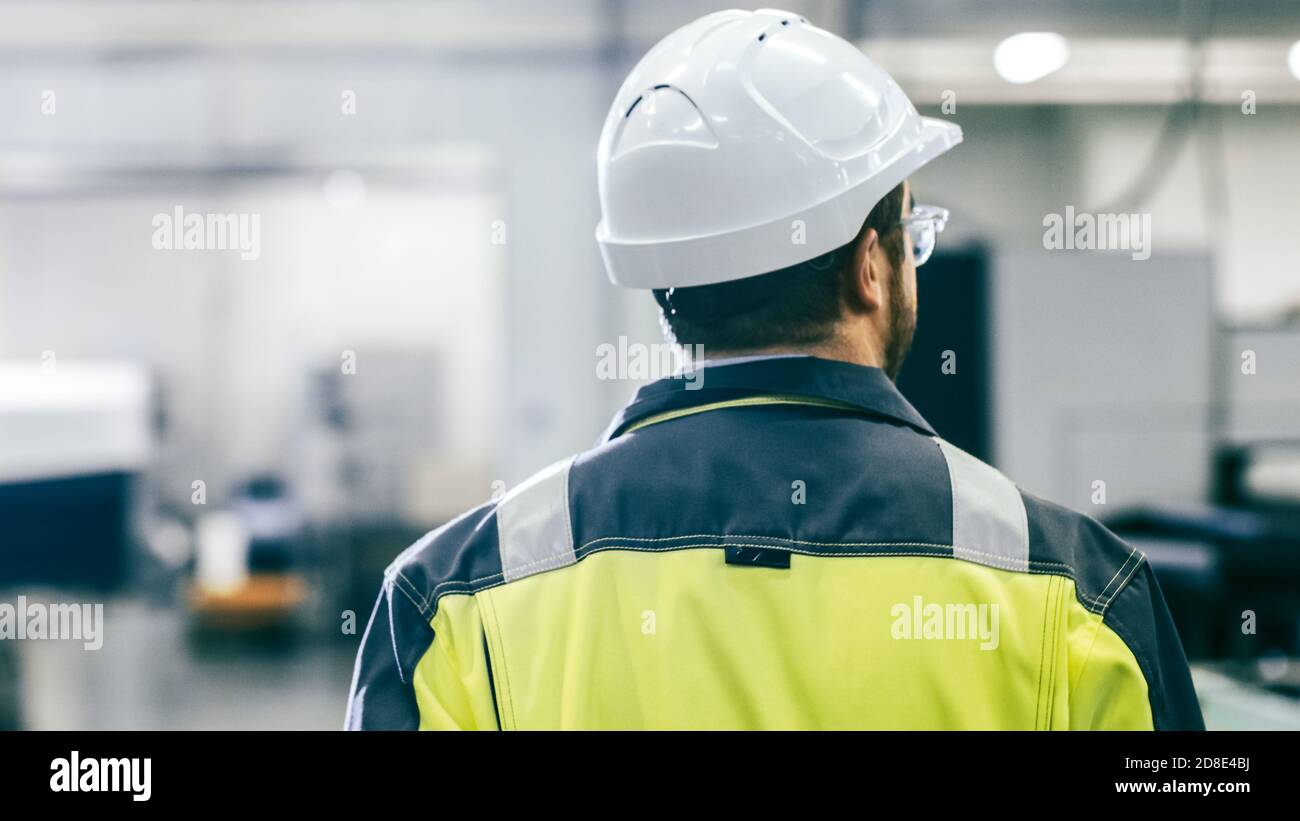 Indietro Vista Foto dell'ingegnere industriale che indossa indumenti protettivi Attraversa il moderno stabilimento di produzione con macchine automatiche in funzione Foto Stock