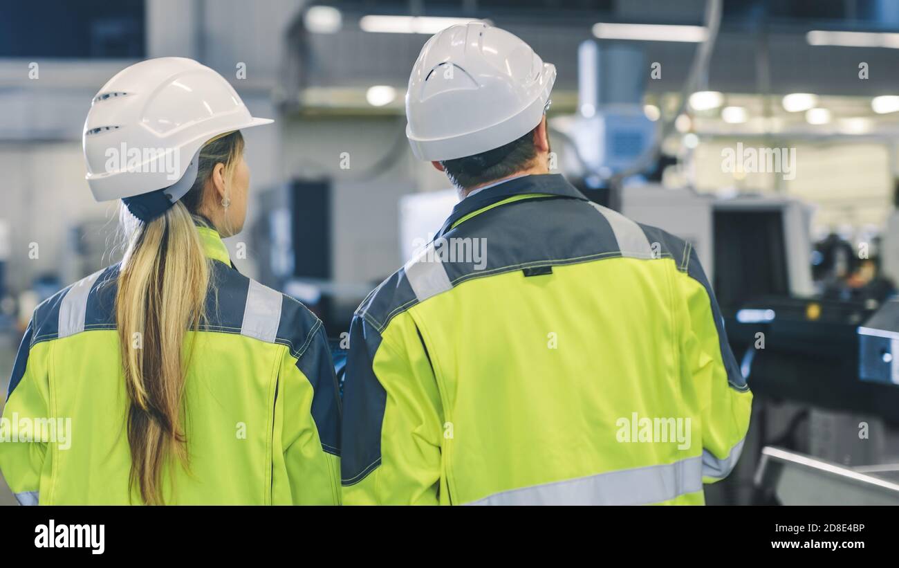 Il lavoratore industriale maschile e il capo ingegnere meccanico femminile a piedi attraverso lo stabilimento di produzione mentre discutono il nuovo progetto della fabbrica. La struttura ha Foto Stock