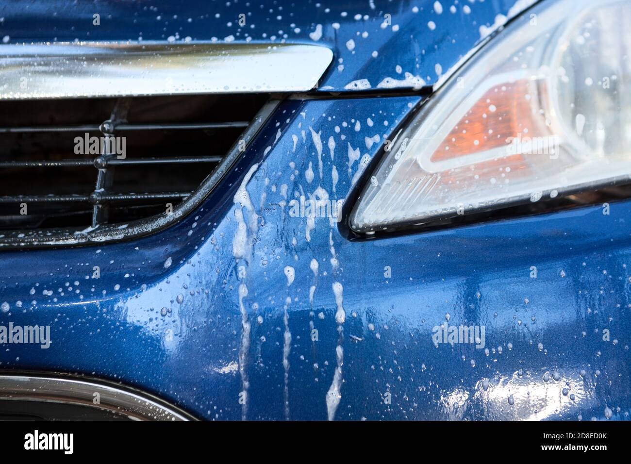 Faro e griglia per auto con schiuma durante il lavaggio dell'auto, vista ravvicinata Foto Stock