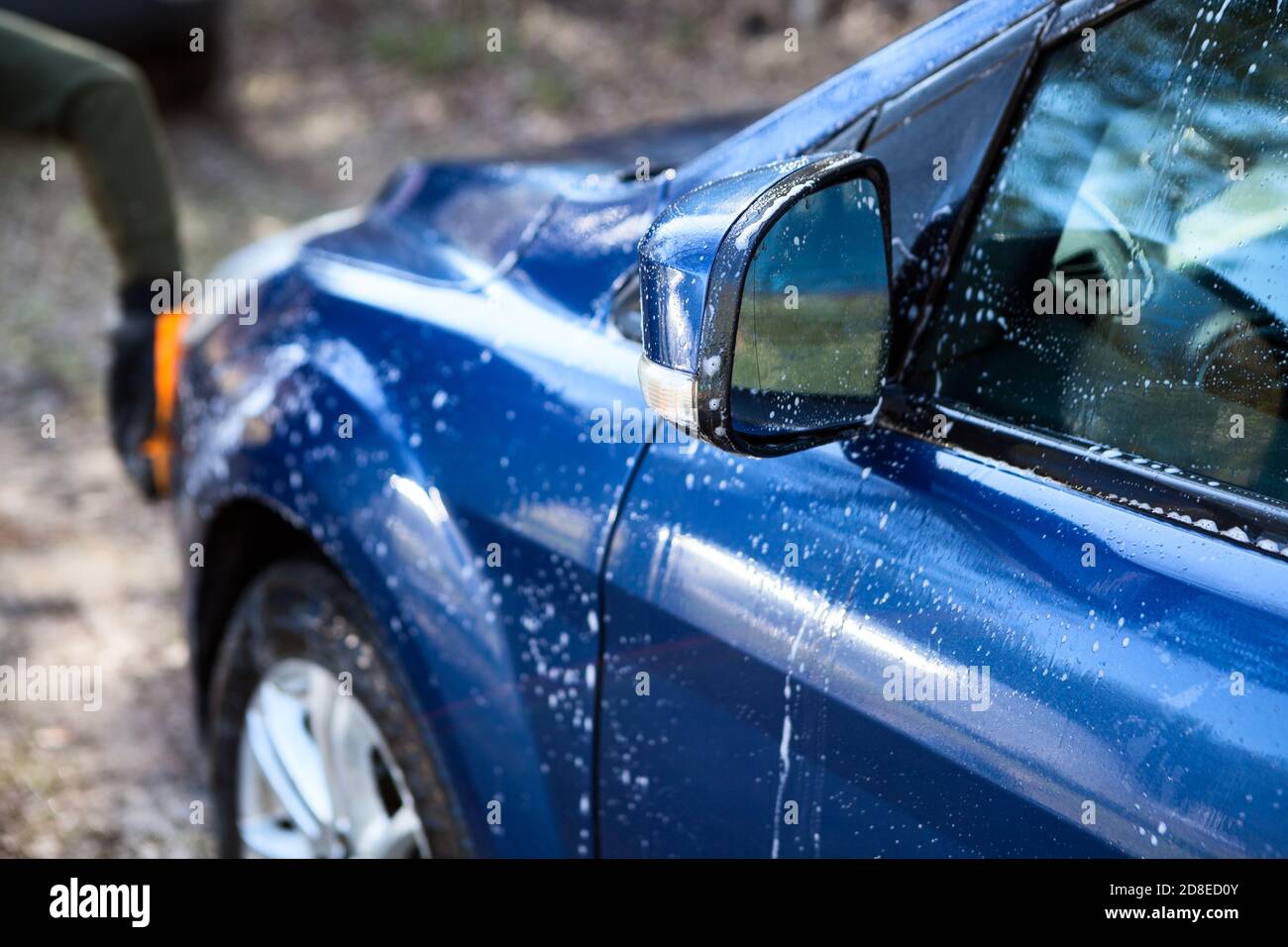 Persona che lava la sua auto con mitten in microfibra, acqua calda e sapone liquido, vista ravvicinata Foto Stock