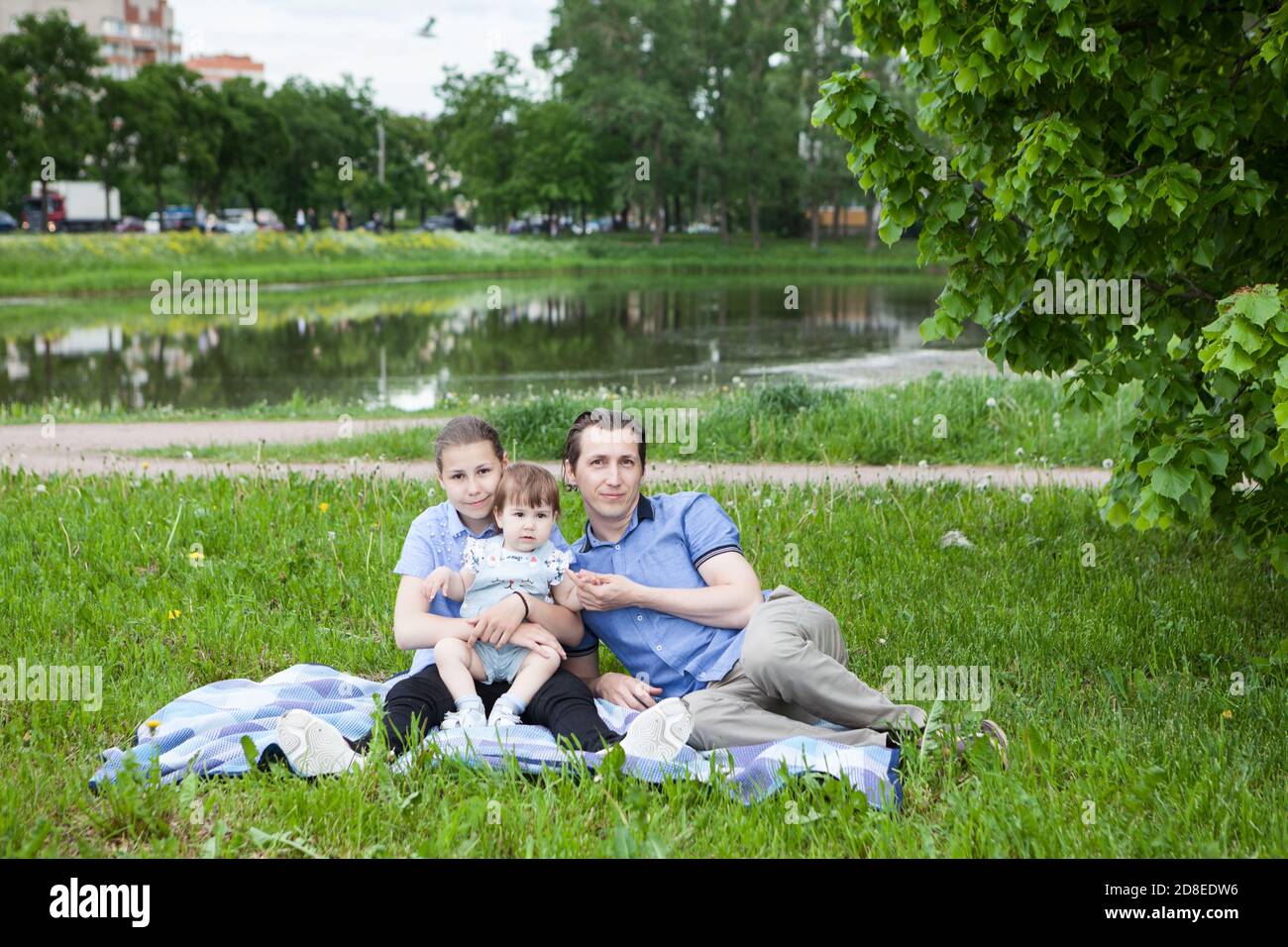 Un solo padre con due figlie è seduto su una coperta d'erba in un parco urbano, bambine e adolescenti Foto Stock
