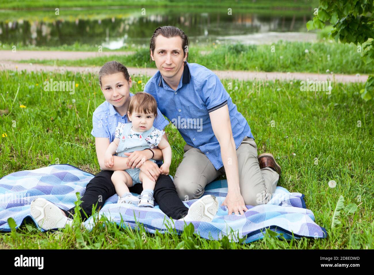 Singolo padre e due figlie seduti su coperta sul prato in un parco urbano, bambino e ragazza adolescente, ritratto all'aperto Foto Stock