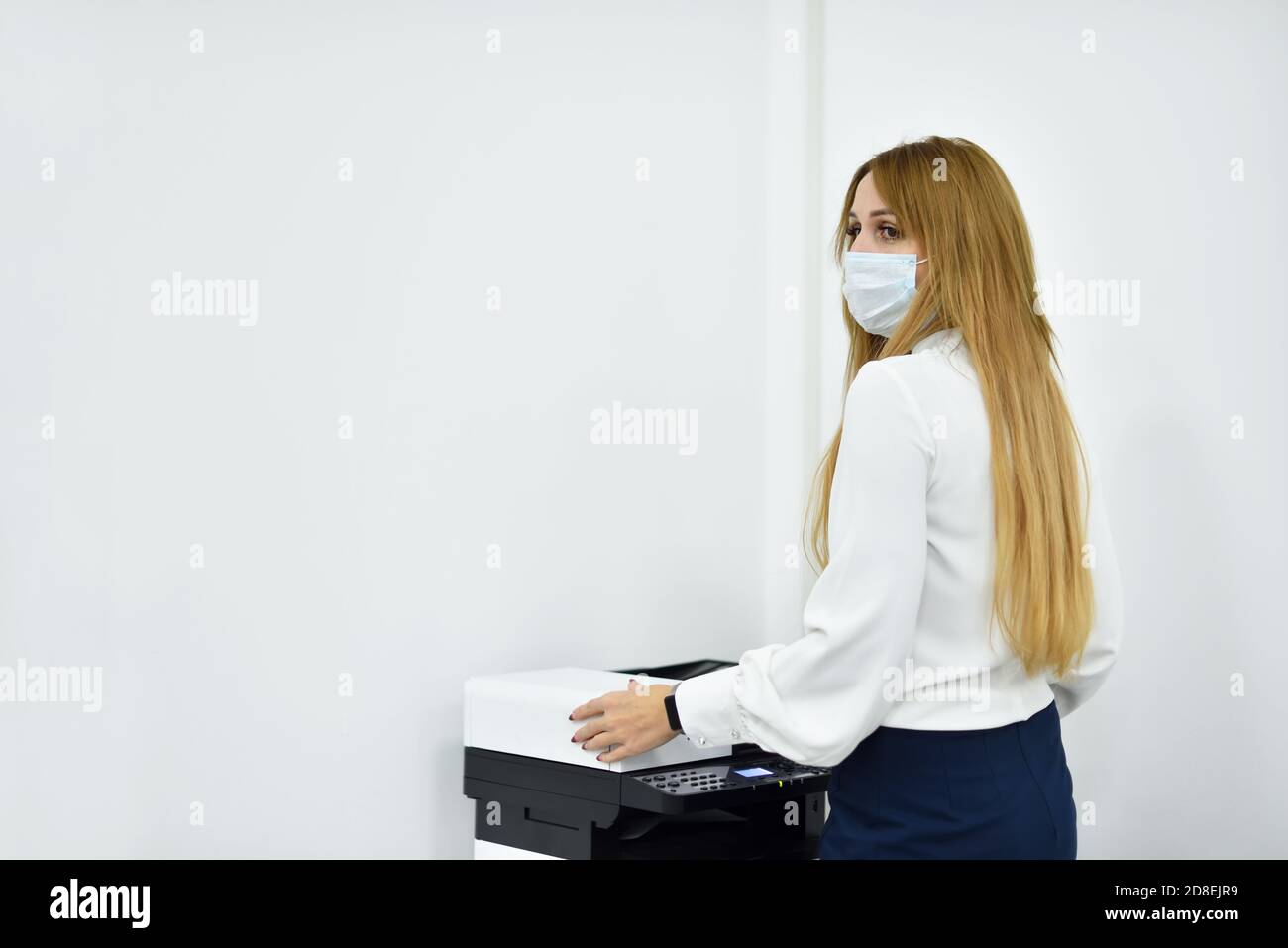 30s donna ufficio Manager in una maschera faccia fa copie di documenti su una copiatrice Foto Stock