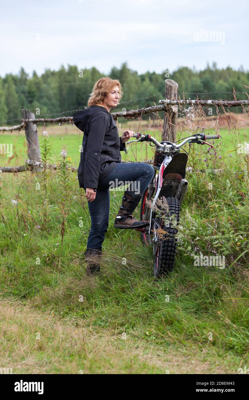 Countrywoman matura in piedi con moto sterrato su strada rurale vicino recinzione Foto Stock