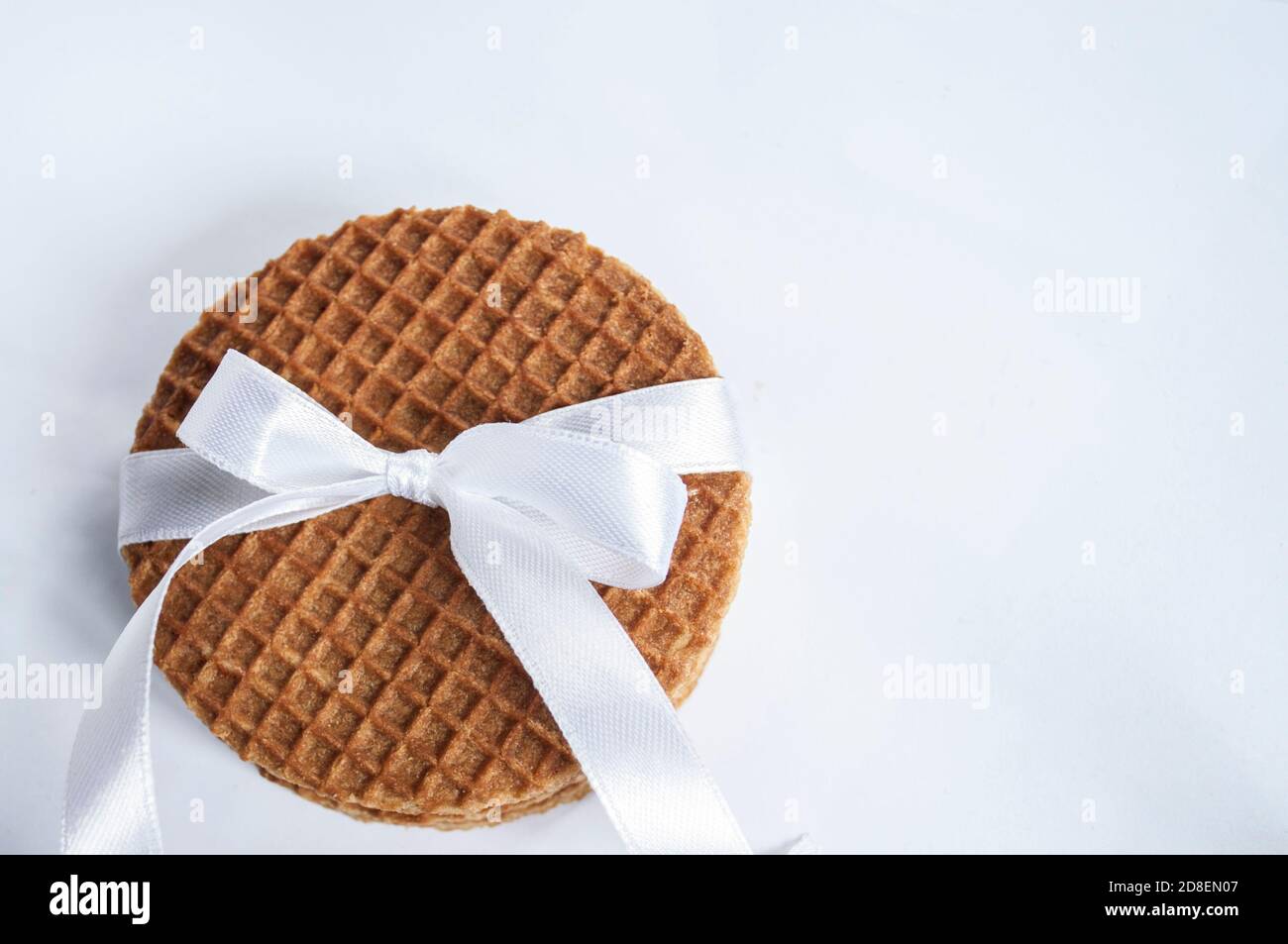 Pila di cialde tonde con caramello nell'angolo in basso a sinistra, con nastro regalo bianco, inchino su sfondo bianco, con spazio per il testo. Messa a fuoco selettiva Foto Stock